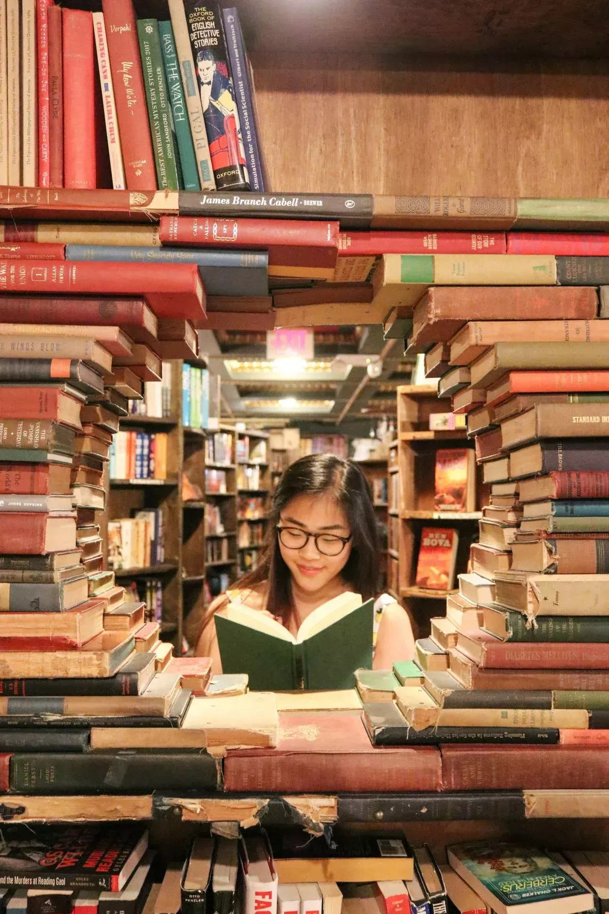 Jeune personne lisant un livre dans une librairie Accompagnement scolaire : une jeune personne trouve son chemin dans les livres, symbole d'une réconciliation avec l'apprentissage.